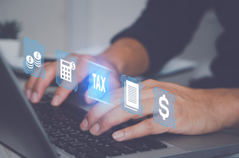 Manos escribiendo en una computadora portátil, con símbolos de impuestos y finanzas.